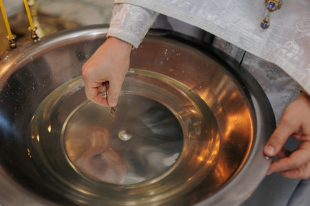 Closeup view to the priest hand holding cross and baptismal font with water. Ceremony of the baptism...