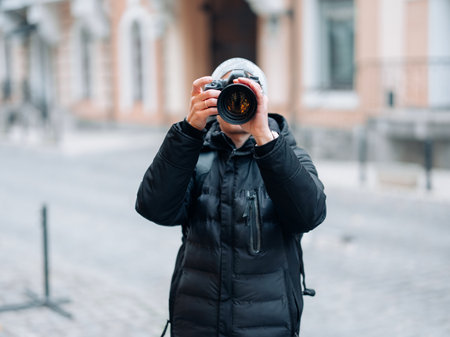 Male photographer takes a photo using professional digital camera against background of city street.の写真素材