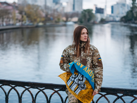 Ukrainian woman soldier holding flag with signatures of Ukrainian warriors and resting in park on vacation. Translation from Ukrainian: Armed Forces of Ukraine, Glory to Ukraine, surname.の写真素材