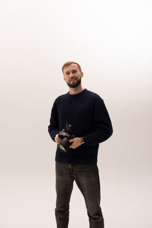 Handsome smiling young photographer holding professional digital camera over white background in...