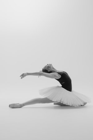 Young ballerina in elegance tutu and pointe shoes dancing against white background. Graceful beautiful ballerina. Ballet art, grace, flexibility, motion. Black and white image.の写真素材