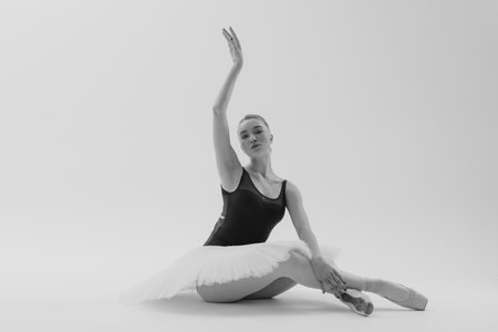 Young ballerina in elegance tutu and pointe shoes dancing against white background. Graceful...
