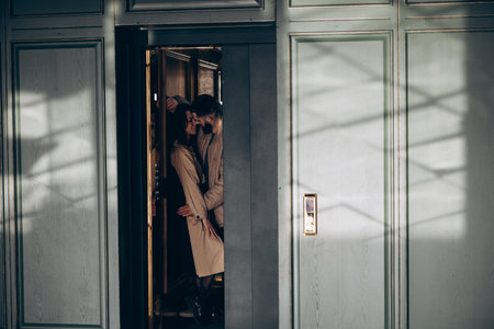 Happy young couple standing inside elevator cabin and embracing against background of buttons.