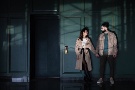 Happy young couple standing inside of building near elevator door, looking each other and holding hands.の写真素材
