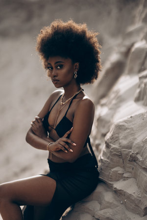 Pretty young African woman posing in black bra and skirt sitting in sandy canyon. Closeup.の写真素材