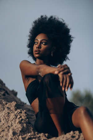 Pretty young African woman posing in black bra and skirt against background of sand and blue sky. Closeup.の写真素材