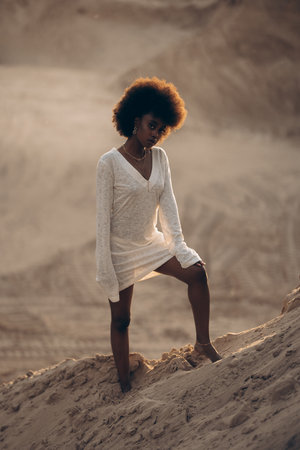 Pretty young African woman posing in white dress in sandy canyon at sunset. Backlit.の写真素材