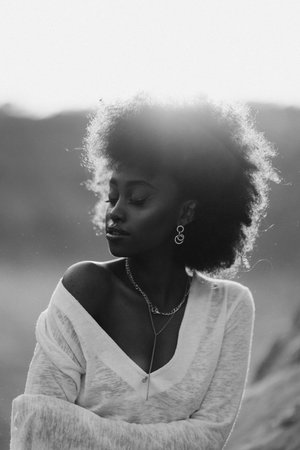 Portrait of young African woman with closed eyes posing outdoor at sunset. Image with backlit. Black and white image.の写真素材