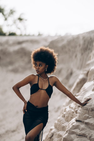 Pretty young African woman posing in black bra and skirt against background of sandy canyon.の写真素材