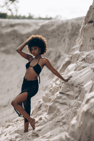 Pretty young African woman posing in black bra and skirt against background of sandy canyon.の写真素材