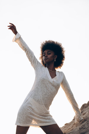 Pretty young African woman posing in white dress against background of sky. Bottom view. Silhouette against sky.の写真素材