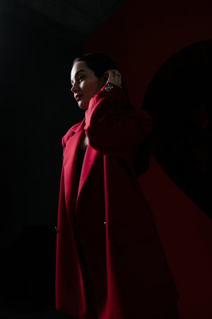 Girl in red jacket illuminated by light posing on black background.の写真素材