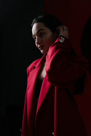 Beautiful girl in red jacket illuminated by light posing on black background. Portrait.の写真素材
