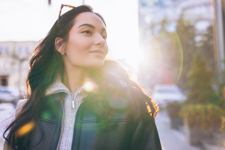 Portrait of young pretty woman in sweater and jacket on city street at sunset. Backlit.の写真素材