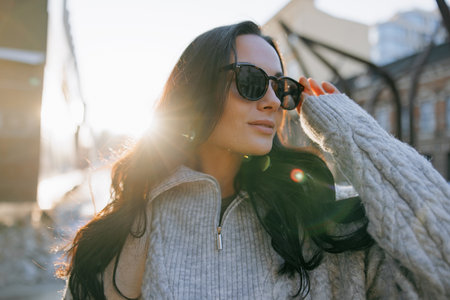 Portrait of young pretty woman in sweater and sunglasses on city street at sunset. Backlit.の写真素材