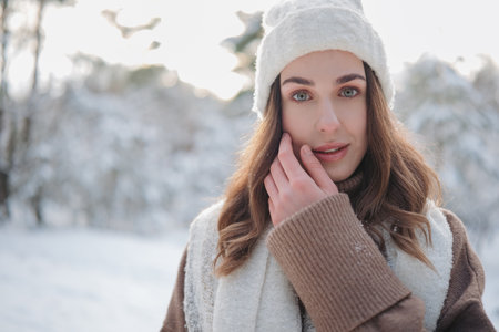 Portrait of young beautiful woman in jacket, scarf and hat during walk in winter forest against background of snow covered trees.の写真素材