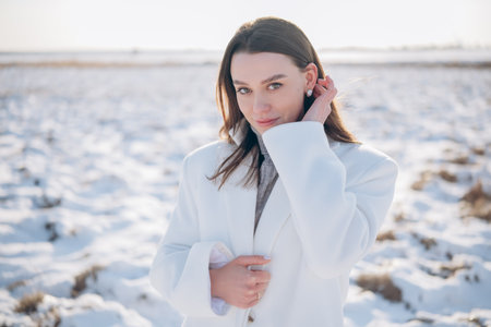 Portrait of young brunette woman in white coat among snow covered meadow during walk in winter day.の写真素材