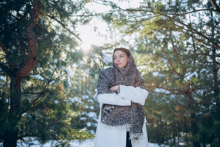Happy young brunette woman wrapped in scarf walking among snow covered pine trees in cold winter day. Close-up.の写真素材