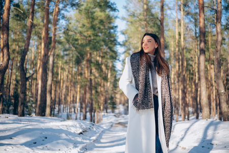 Happy young brunette woman enjoying by snowy forest and walking on forest road among pine trees in winter sunny day. Close-up.の写真素材