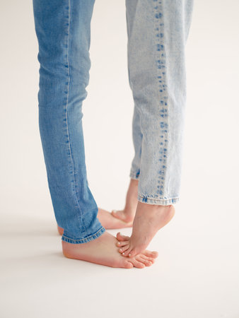 Close-up of a romantic couple of man and woman standing barefoot in jeans, gently embracing on light background. Intimate and tender moment, concept of love, connection, and relationship.の写真素材
