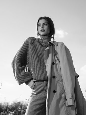 Young woman with trench coat stands against background of sky and clouds. Close-up and bottom view. Black and white image.の写真素材