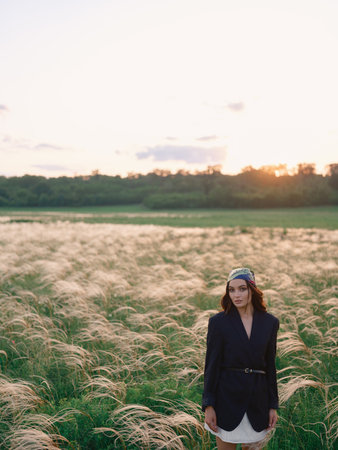 Young woman walking among feathergrass in steppe at sunset against beautiful landscape. Summer outdoor scene with feather grass in steppe in Ukraine. Backlit.の写真素材