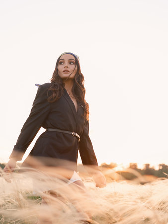 Young woman walking among feathergrass in steppe at sunset against sky background. Summer outdoor scene with feather grass in steppe in Ukraine. Backlit and close-up. Bottom view.の写真素材