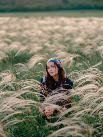 Young woman sitting and relaxing among feathergrass in steppe against beautiful landscape. Summer outdoor scene with feather grass in steppe in Ukraine. Close-up.の写真素材