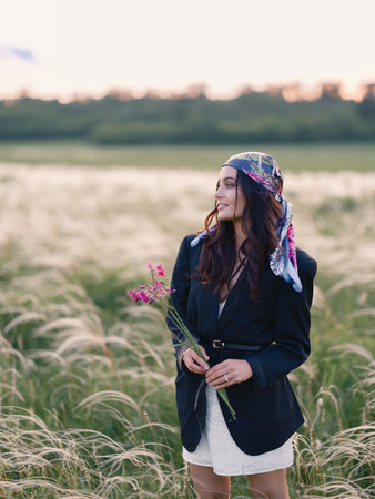 Young woman enjoying and walking among feathergrass in steppe with bouquet of wild gladiolus in her hands at sunset against beautiful landscape. Summer outdoor scene in Ukraine. Close-up.の写真素材
