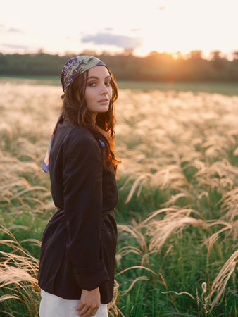 Young woman walking among feathergrass in steppe at sunset against beautiful landscape. Summer outdoor scene with feather grass in steppe in Ukraine. Backlit. Close-up.の写真素材