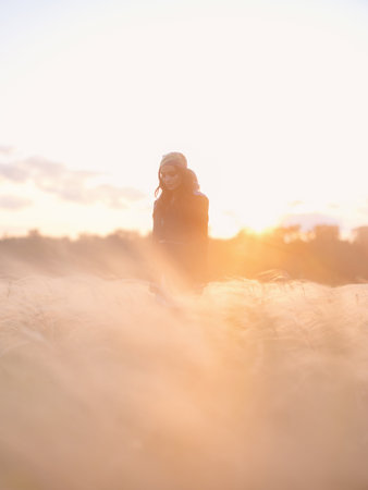 Young woman walking among feathergrass in steppe at sunset against beautiful landscape. Summer outdoor scene with feather grass in steppe in Ukraine. Backlit.の写真素材