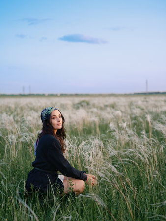 Young woman sitting and relaxing among feathergrass in steppe against beautiful landscape with blue sky. Summer outdoor scene with feather grass in steppe in Ukraine. Close-up.の写真素材