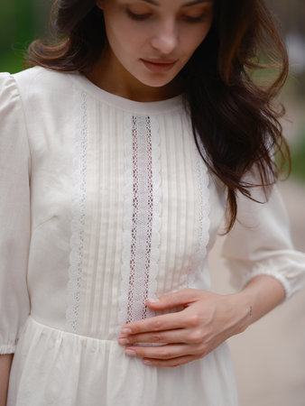 Portrait of young woman in white dress with lace standing against blur background of forest. Close-up. Calm natural setting, peaceful atmosphere, and soft daylight.の写真素材