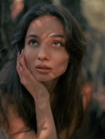 Portrait of young brunette woman with long hair and shadow on her face dreaming and relaxing in the...