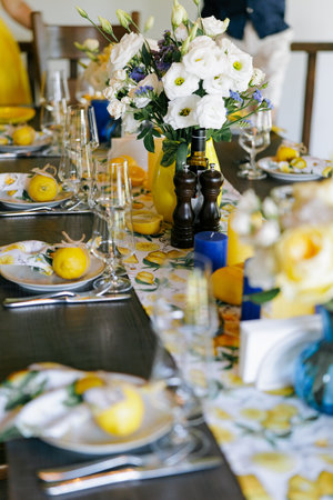 Stylish dining table decorated with bright yellow lemons, white flowers, and elegant tableware. Fresh floral centerpiece, rustic yet modern design. Festive summer celebration or wedding banquet.の写真素材