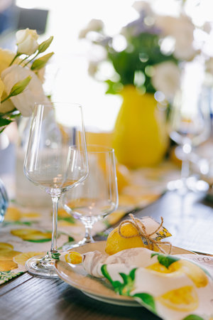 Stylish dining table decorated with lemons, white flowers, and elegant tableware. Fresh floral centerpiece, rustic yet modern design. Festive summer celebration or wedding banquet. Close-up.の写真素材