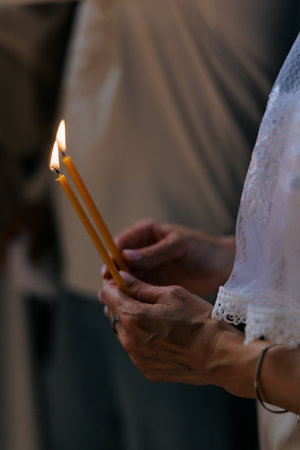 Hands of woman holding burning wax candles in the Orthodox Church during a church service. Closeup.の写真素材