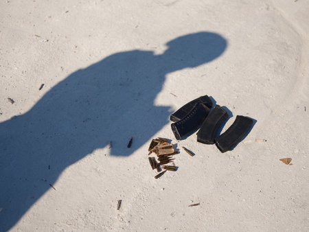 Pile of rifle magazines and scattered ammunition on the white ground. Symbolic image of the tools of war under the shadow of a human presence. War in Ukraine.の写真素材