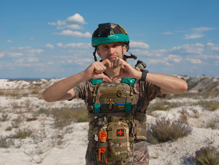 Portrait of a Ukrainian soldier in a tactical vest making a heart sign with his hands. The gesture symbolizes love and dedication to his homeland. War in Ukraine.の写真素材