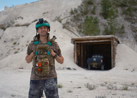 Portrait of Ukrainian soldier in tactical gear with a body camera, smiling at the camera. In the...