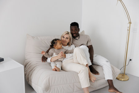 Happy biracial family relaxing on a comfortable sofa in a bright, minimalist studio. Concept of interracial family.の写真素材