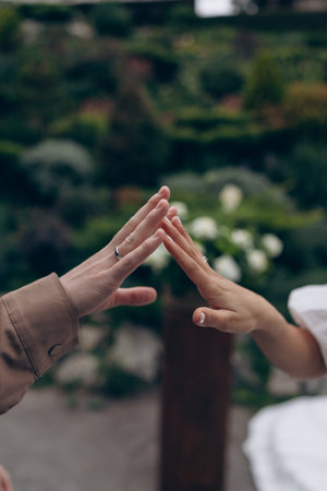 Close-up of a couple hands reaching and meeting in a gentle touch, forming a shape of a roof or...