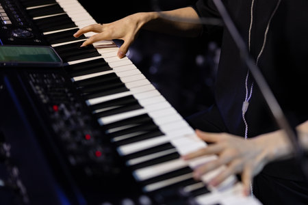 Close-up of a musician's hands playing the black and white keys of a digital piano or synthesizer keyboard during a live performance or recording session.の写真素材