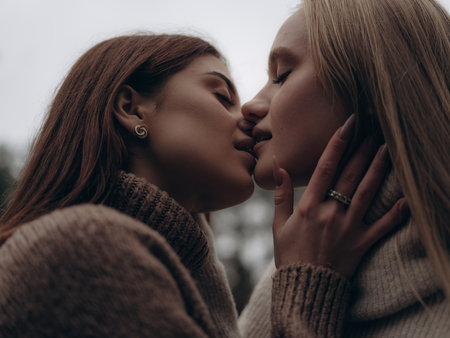 Close-up emotional portrait young lesbian couple kissing tenderly in forest. Hand with engagement ring touches partners face. Showing intimacy, passion, love, and commitment in LGBT relationships.の写真素材