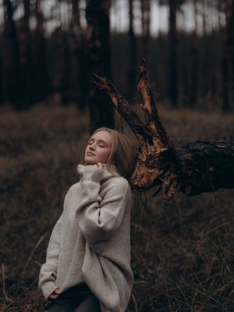 Emotional portrait young blonde woman with eyes closed relaxing or meditating in forest. Serenity, contemplation, fashion, and autumn style.の写真素材