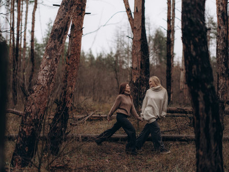 Happy young lesbian couple walking hand in hand through the forest and laughing. Showing joy, fun, movement, and a carefree lifestyle in diverse LGBT relationships.の写真素材