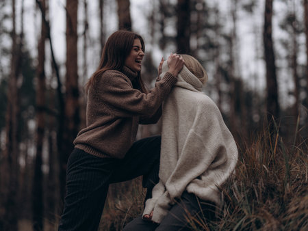 Young lesbian couple laughing frankly, one woman playfully covering partner face with a sweater. Showing fun, joy, and emotional bonding in diverse LGBT relationships.の写真素材