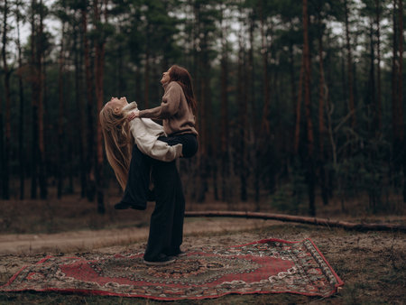 Energetic shot young lesbian couple having fun, laughing, hugging and lifting partner on carpet among forest. Showing powerful joy, fun, physical connection, and happy moment in LGBT relationship.の写真素材