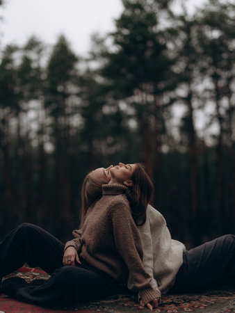 Emotional portrait of young lesbian couple sitting back-to-back on carpet, relaxing and looking up. Showing mutual comfort, support, and deep emotional bond in diverse LGBT relationships.の写真素材