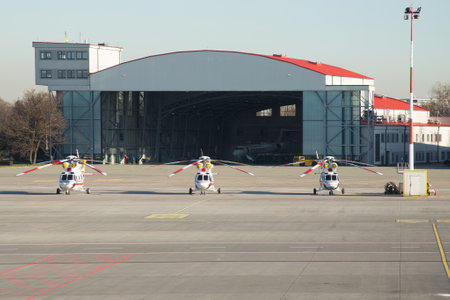 Three helicopters stand in a row. In the background, a hangar with a private airplane. At the airport there are three helicopters.の写真素材